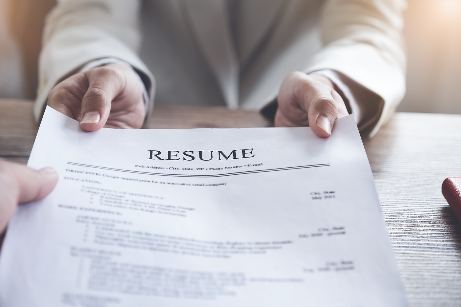 Person handing a resume to someone across a desk.